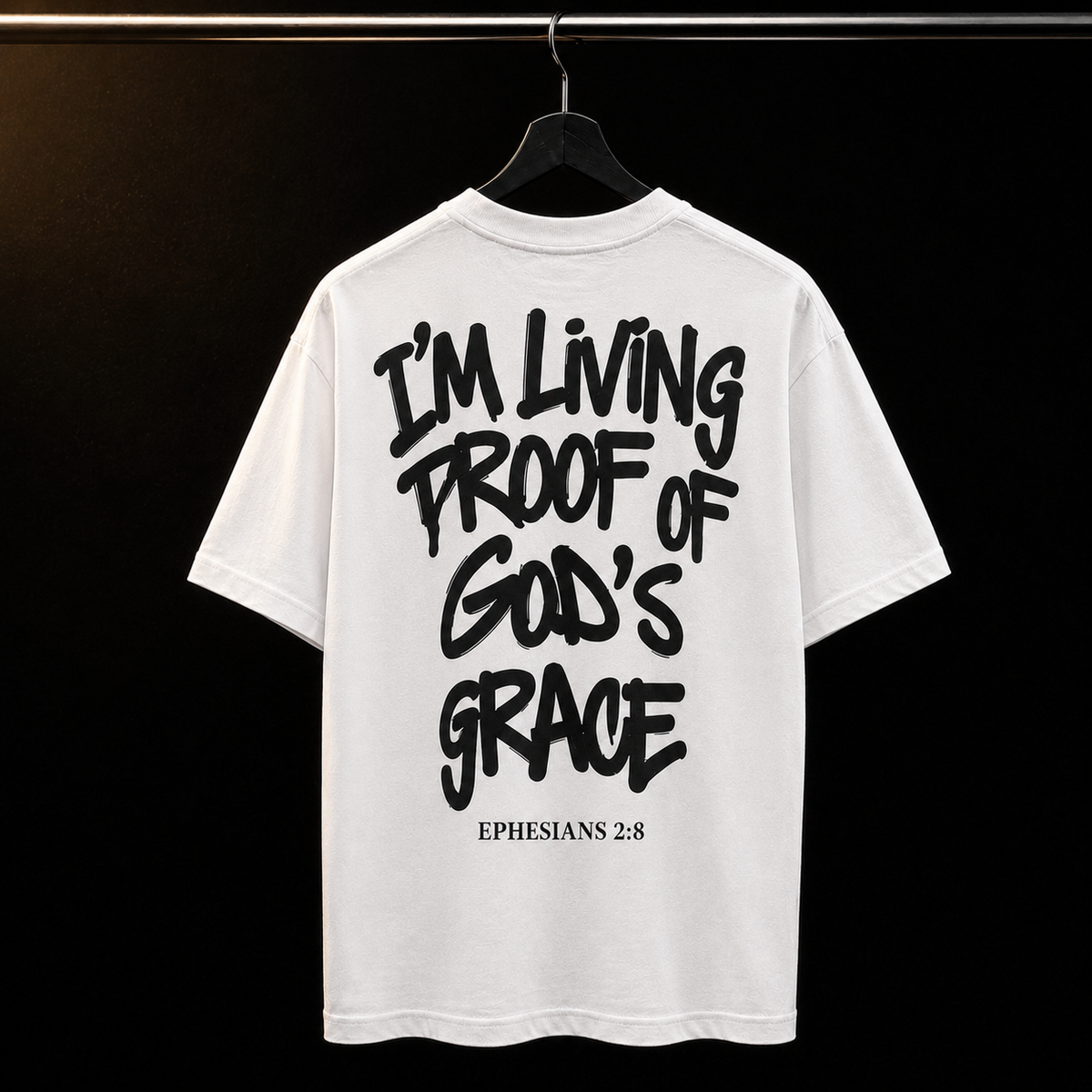White t-shirt with black text 'I'm Living Proof of God's Grace Ephesians 2:8' on a hanger against a black background